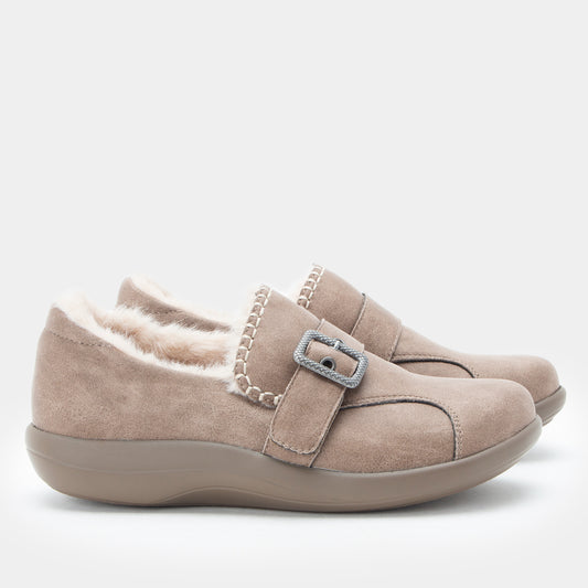 A pair of taupe suede slip-on shoes with a plush cream lining and a decorative silver buckle strap, shown against a light gray background.