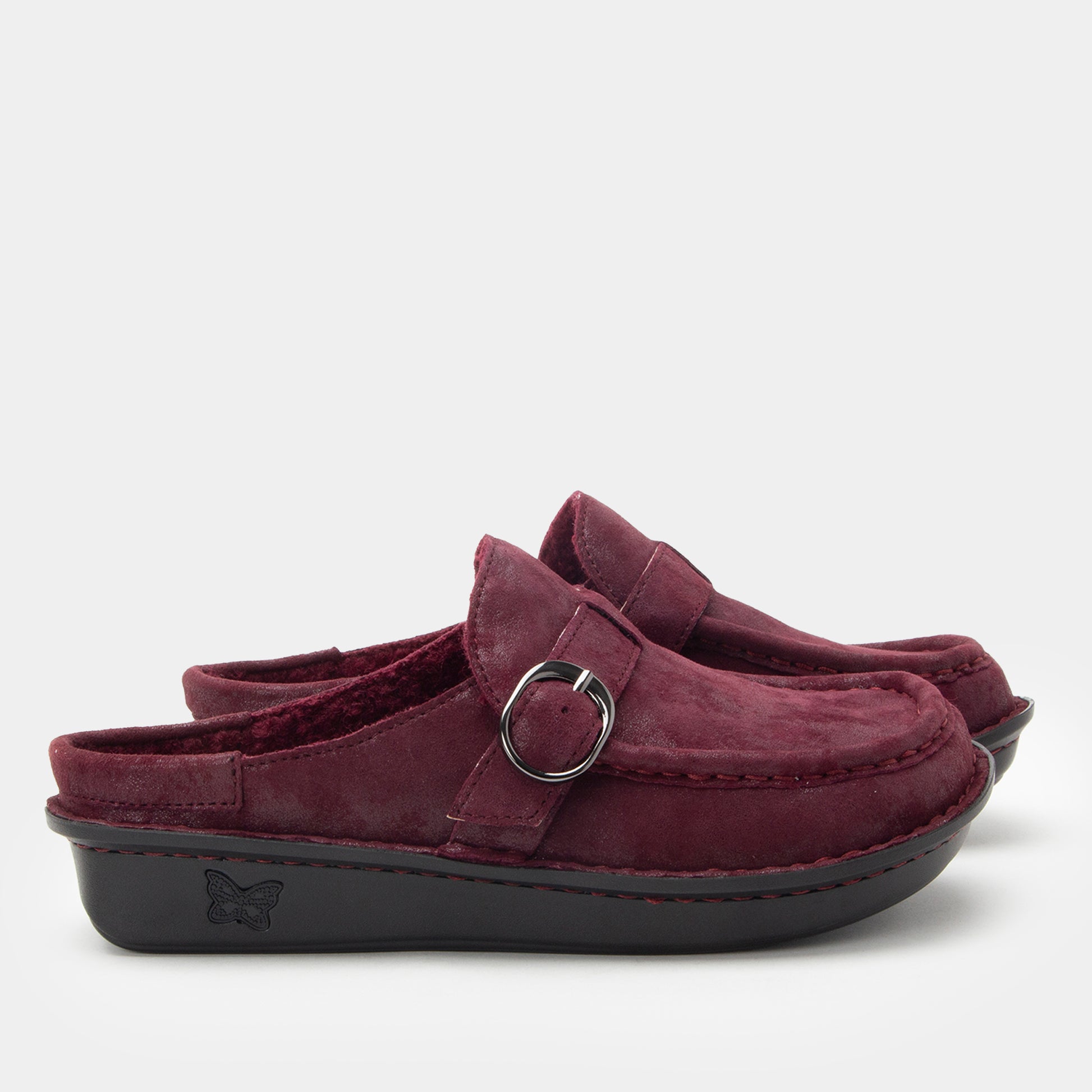 Pair of maroon clogs with a buckle on a light gray background