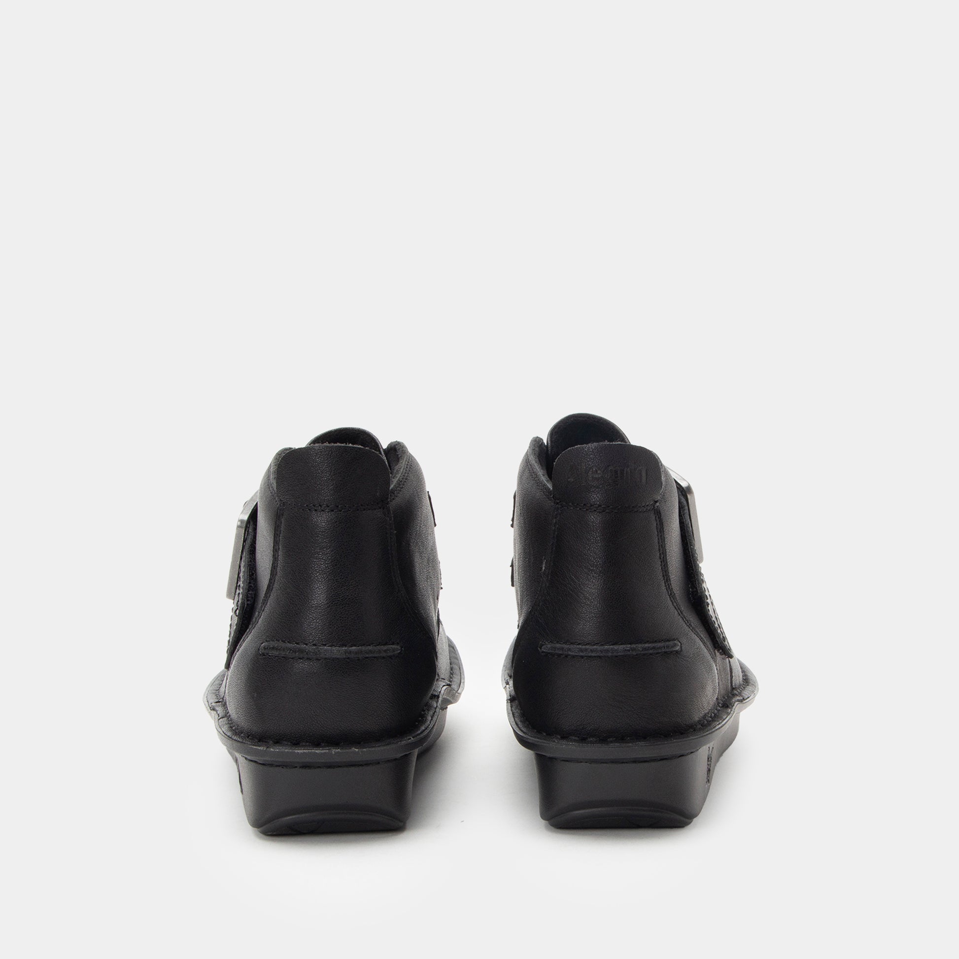 A pair of black leather ankle boots shown from the back, featuring side zippers and low block heels, set against a plain light gray background.