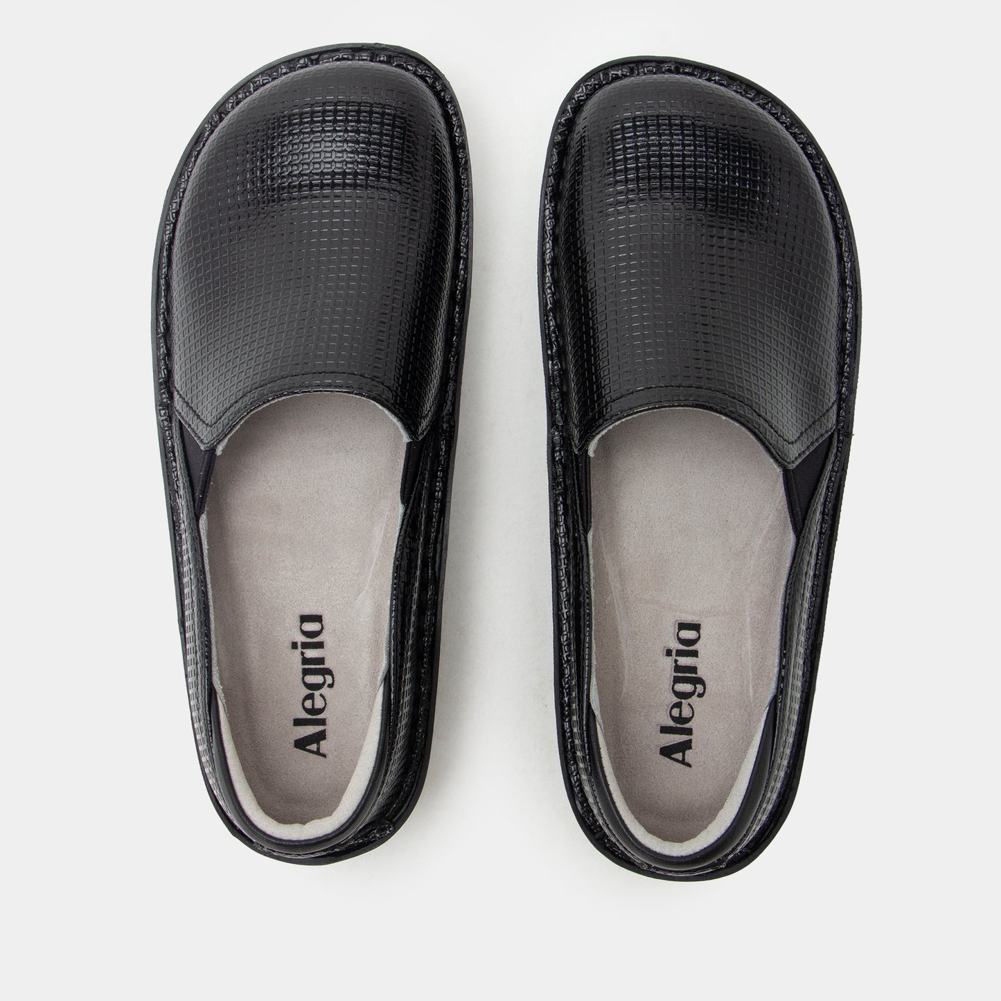 A pair of black slip-on shoes with textured faux-croc uppers and light gray insoles, shown from a top-down view on a light gray background. The brand name 'Alegria' is printed on the insoles.