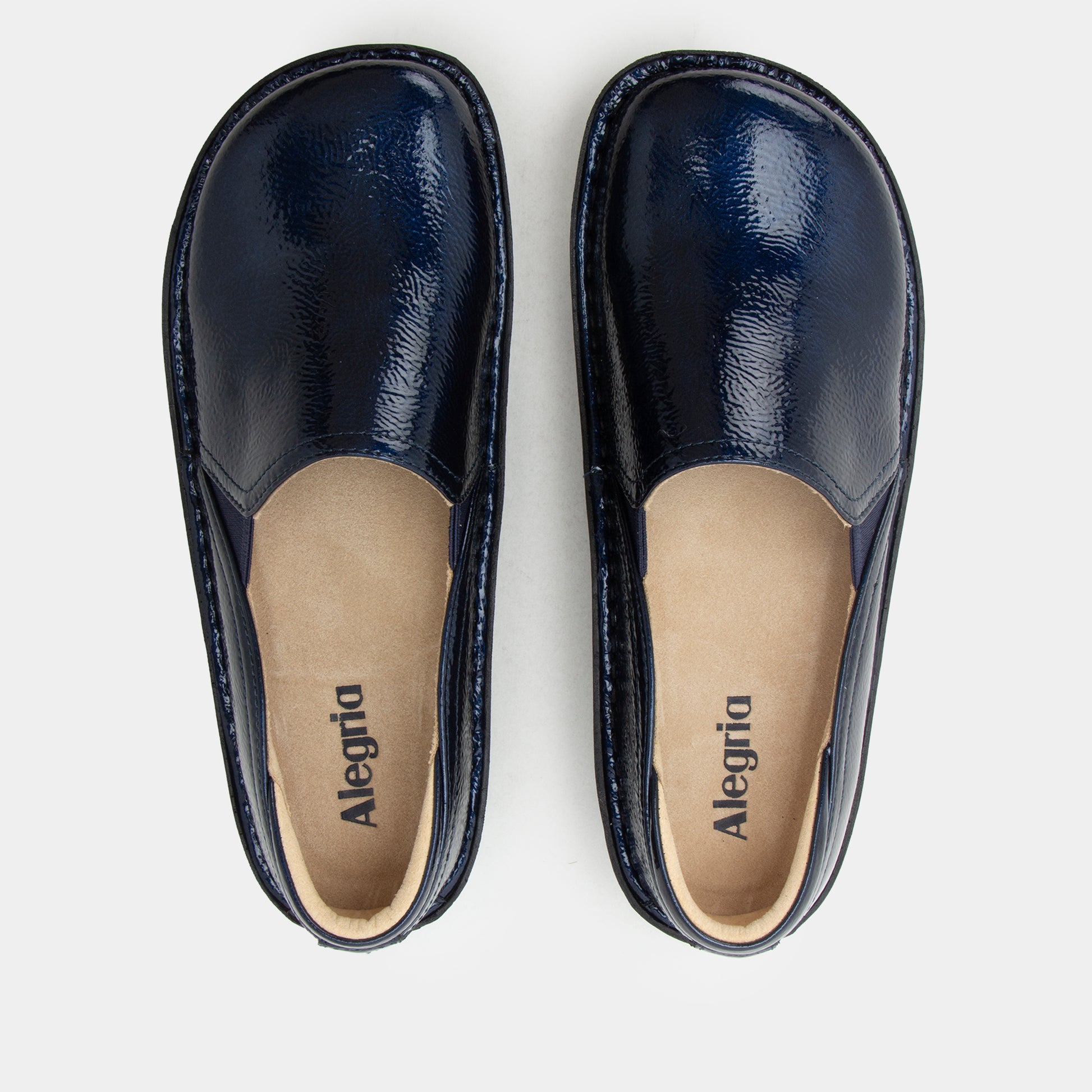 A pair of navy blue leather slip-on shoes with a glossy finish, shown from a top-down view on a light gray background. The beige insoles display the brand name 'Alegria'.