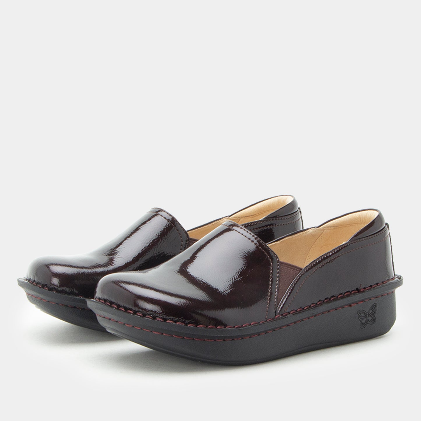 A pair of deep burgundy patent leather slip-on platform shoes with red contrast stitching and a small butterfly logo on the side heel, shown against a light gray background.