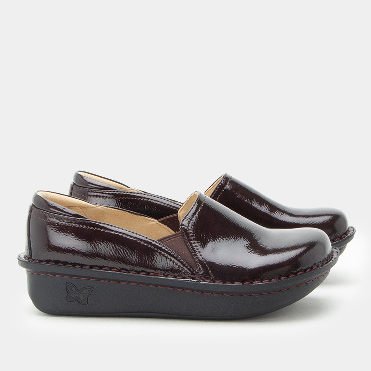 A pair of women's slip-on wedge shoes in glossy deep burgundy patent leather with a black platform sole and a small butterfly logo on the heel, shown against a light gray background.