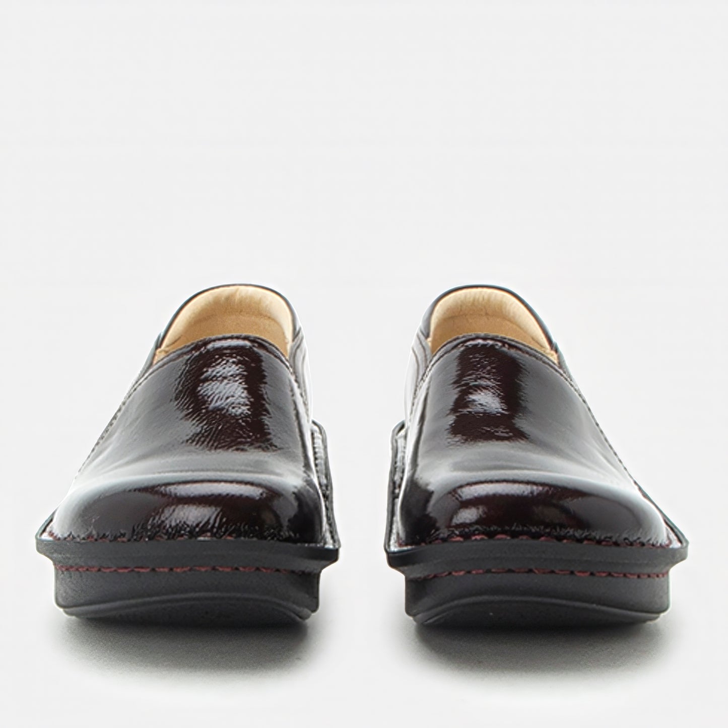 A pair of glossy deep burgundy patent leather slip-on shoes with red contrast stitching and a light tan interior lining, shown from the front on a light gray background.