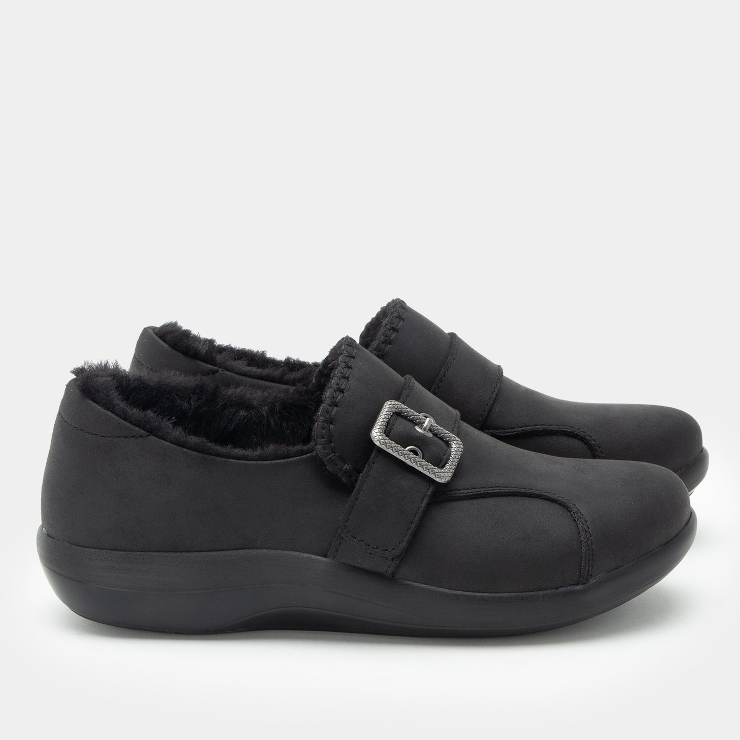 A pair of black slip-on shoes with a plush faux-fur lining and a silver buckle strap, shown against a light gray background.