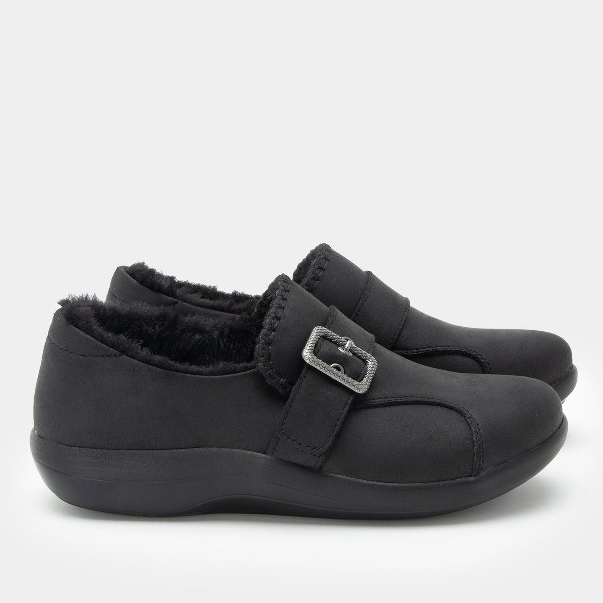 A pair of black slip-on shoes with a plush faux-fur lining and a silver buckle strap, shown against a light gray background.
