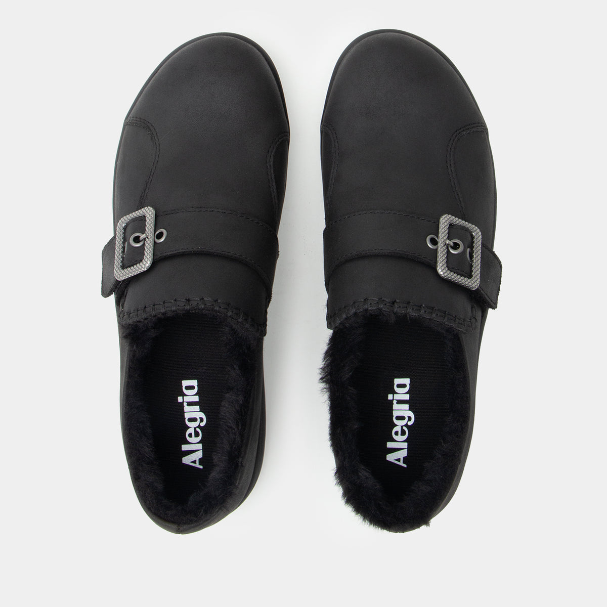 A pair of black slip-on mule shoes with faux fur lining and a silver buckle strap, shown from a top-down view on a light gray background. The brand name 'Alegria' is printed in white on the insole.