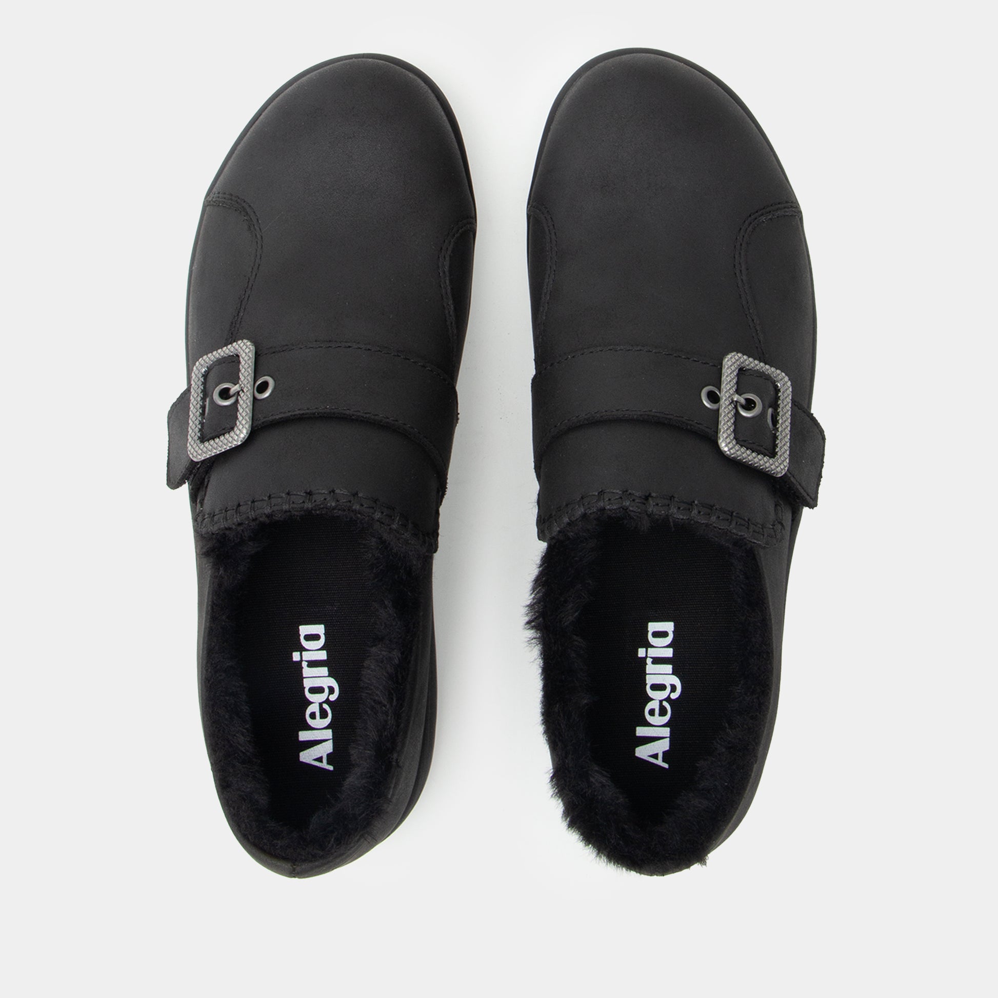 A pair of black slip-on mule shoes with faux fur lining and a silver buckle strap, shown from a top-down view on a light gray background. The brand name 'Alegria' is printed in white on the insole.