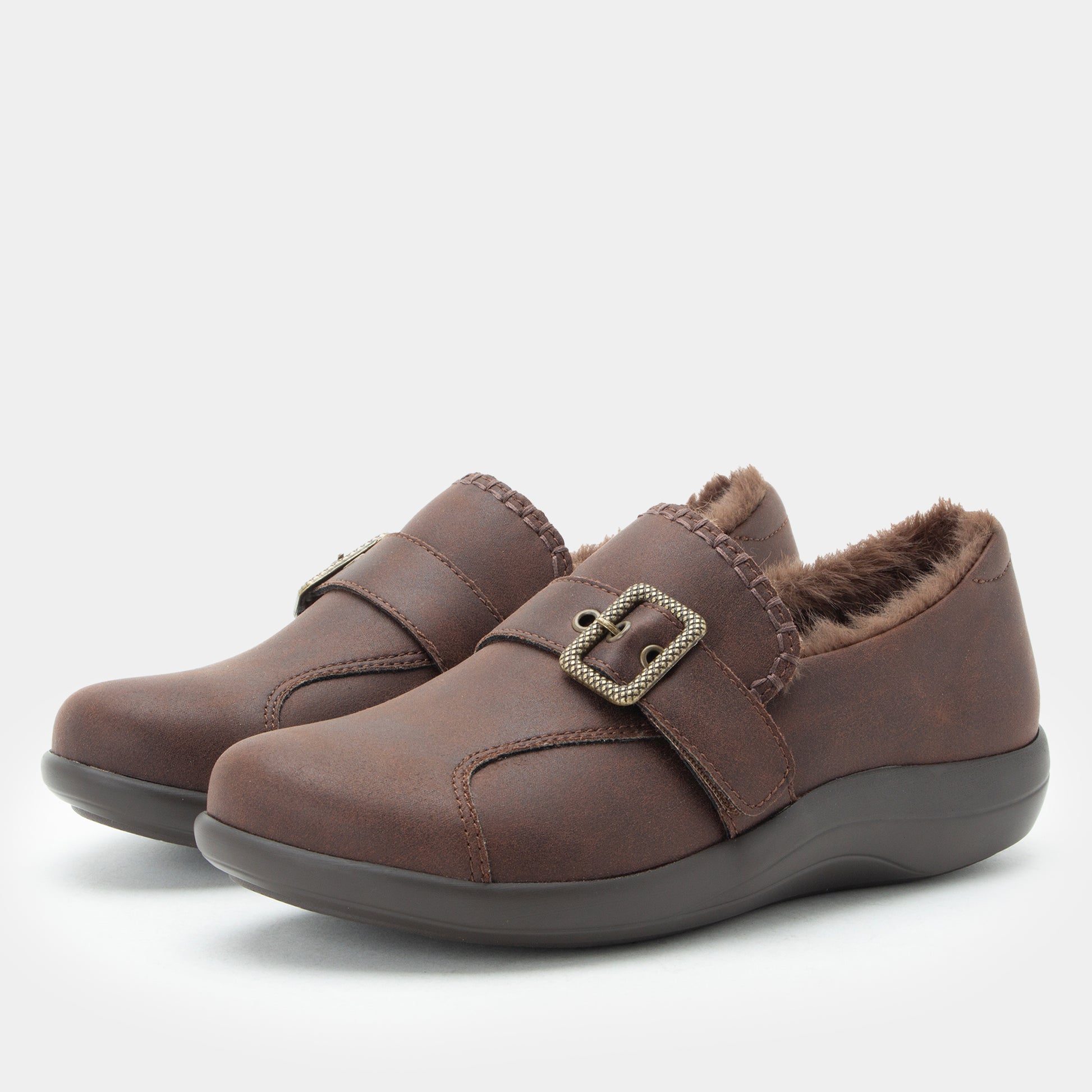 A pair of women's slip-on slipper shoes in dark brown faux leather with a plush brown faux-fur lining and a decorative silver buckle strap, shown on a light gray background.
