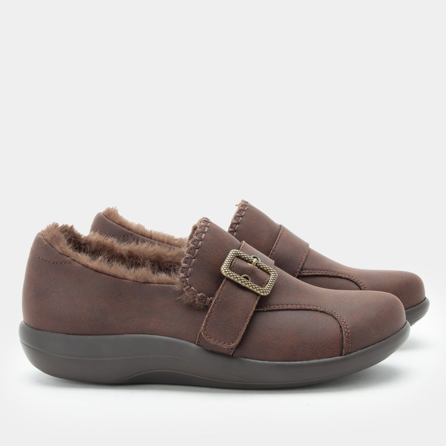 A pair of women's slip-on shoes in dark brown faux leather with a fuzzy brown shearling-style lining and a decorative metal buckle strap, shown against a light gray background.