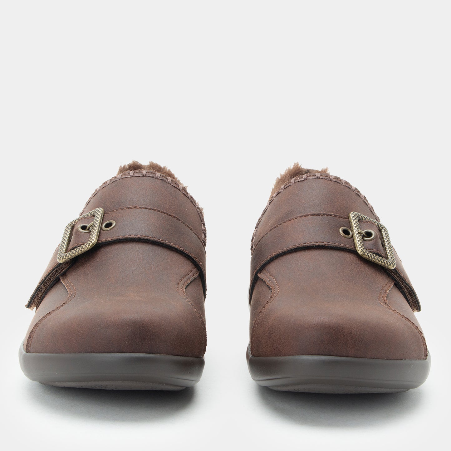 A pair of women's brown slip-on clogs with faux-leather uppers, decorative buckle straps, and soft fuzzy lining visible at the opening, shown against a light gray background.