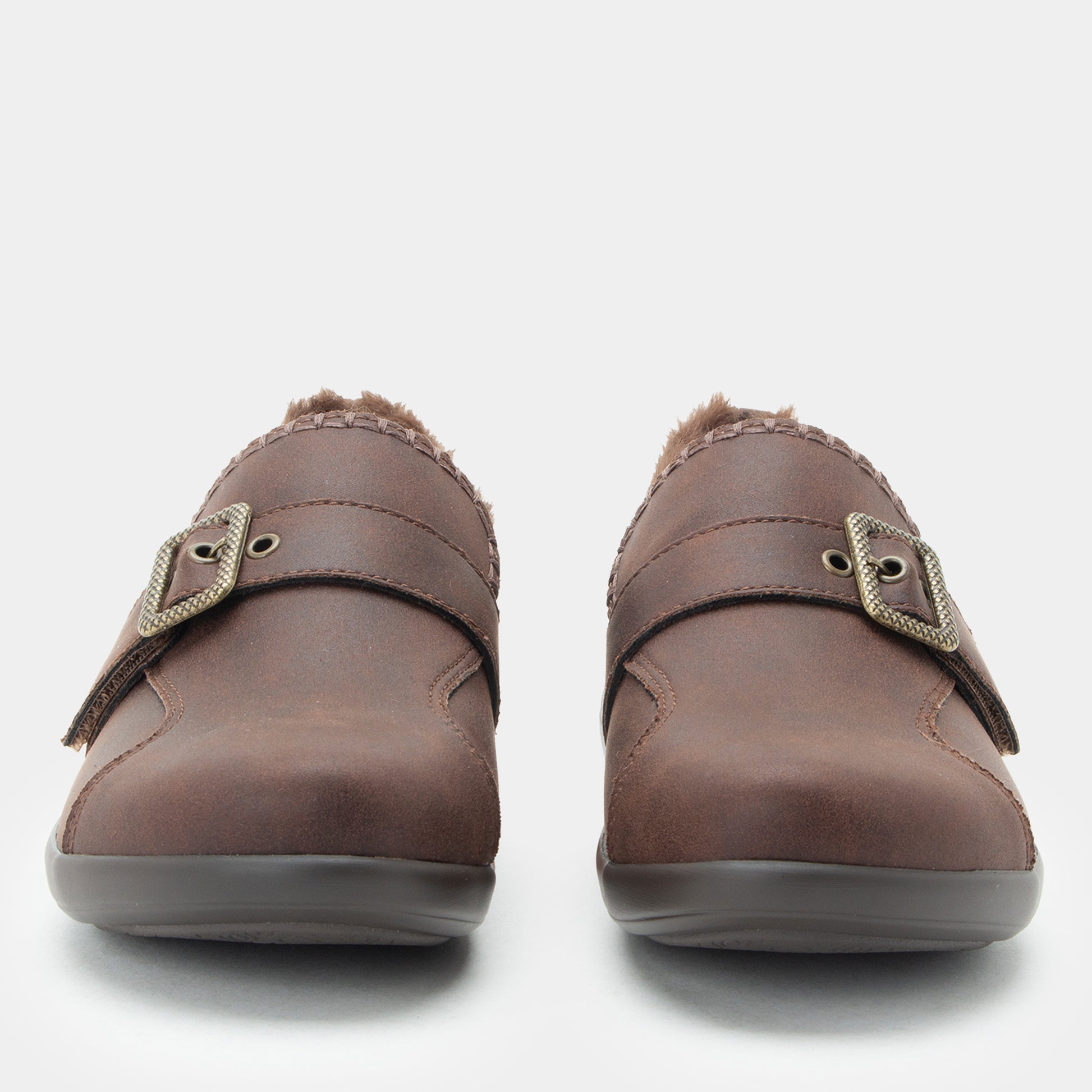 A pair of women's brown slip-on clogs with faux-leather uppers, decorative buckle straps, and soft fuzzy lining visible at the opening, shown against a light gray background.
