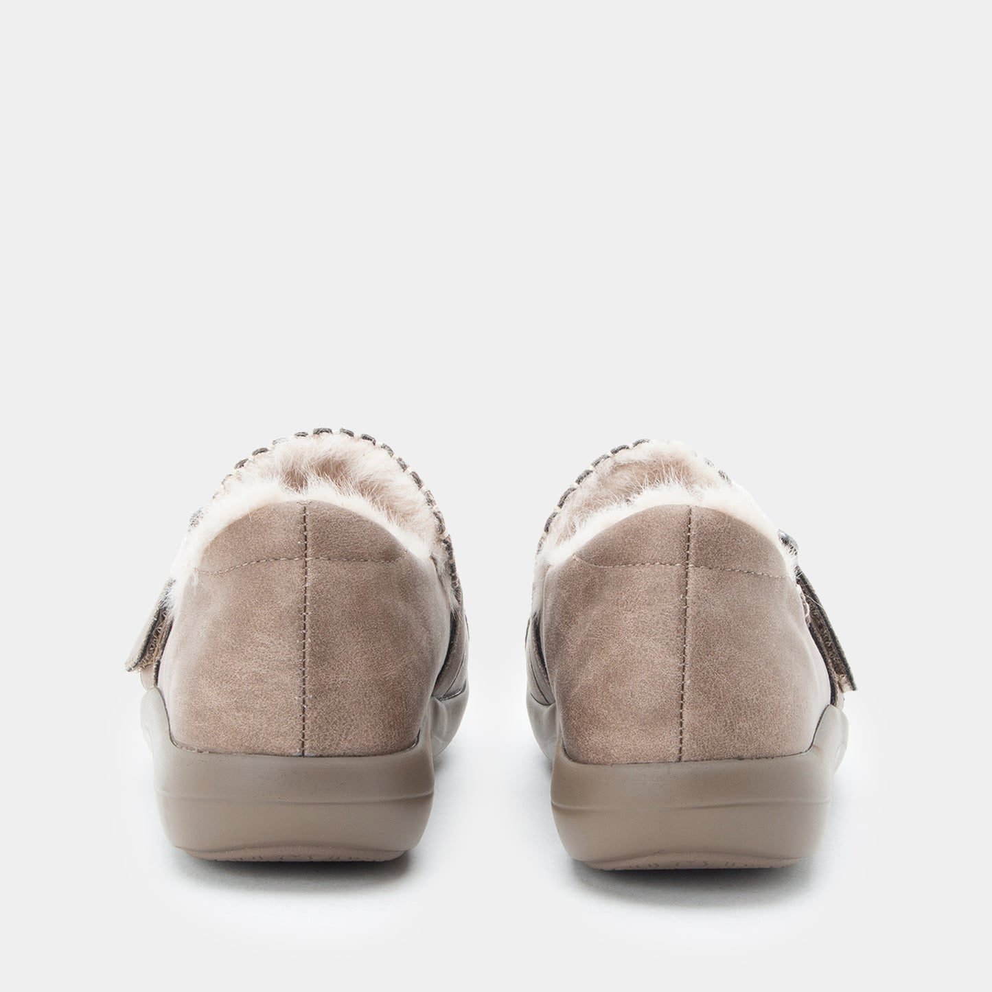 A pair of women's slip-on shoes shown from the back, featuring taupe suede uppers with a soft white shearling-style lining and a matching taupe sole.