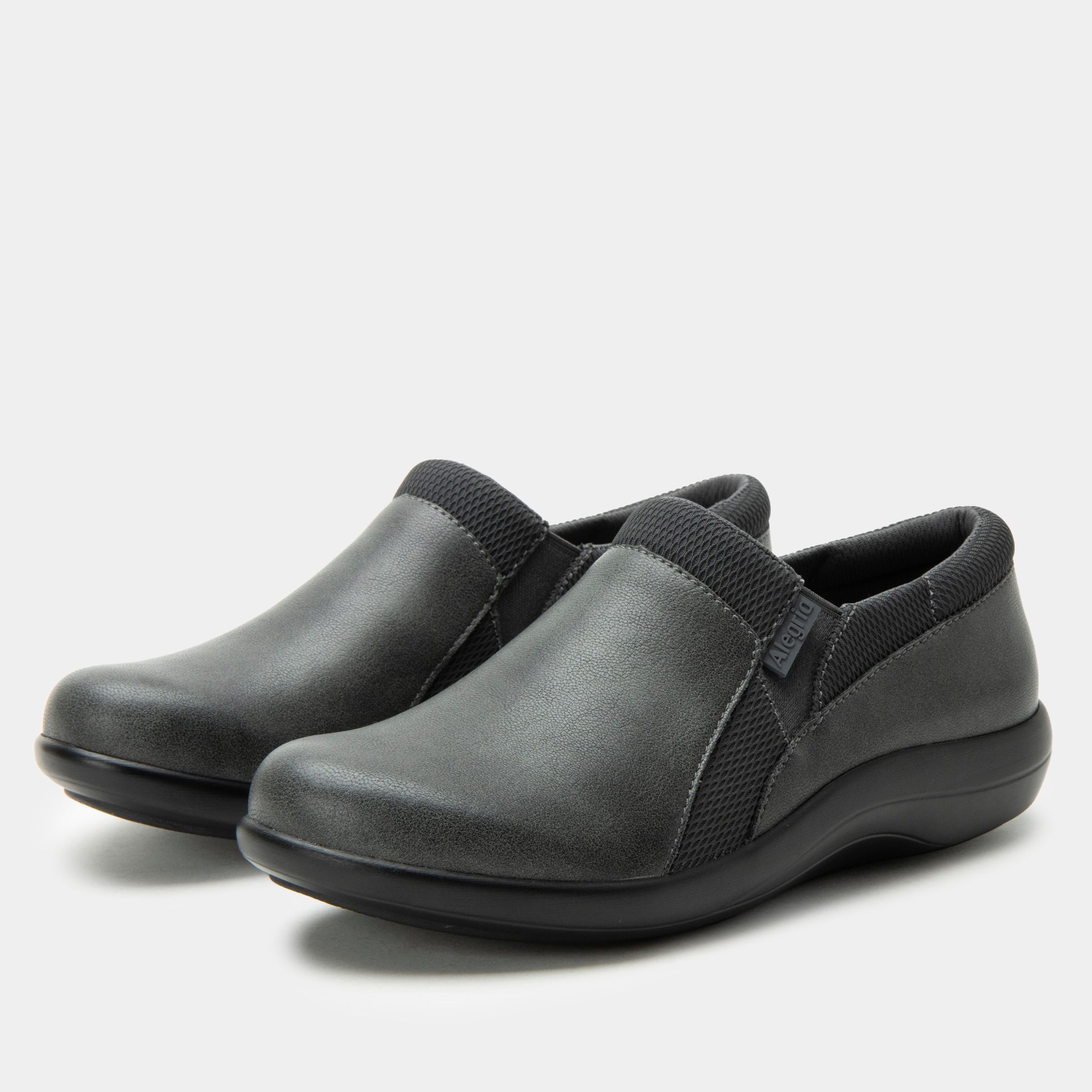 Pair of gray slip-on shoes with black straps on a light gray background