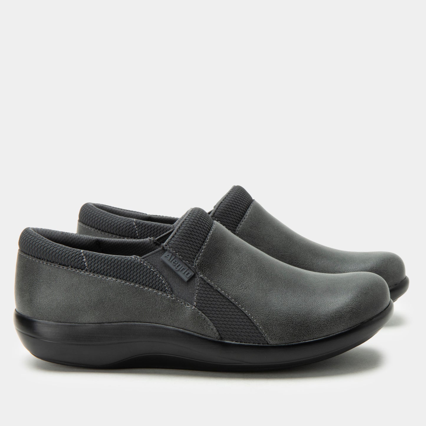 Pair of gray slip-on shoes with black soles on a light gray background