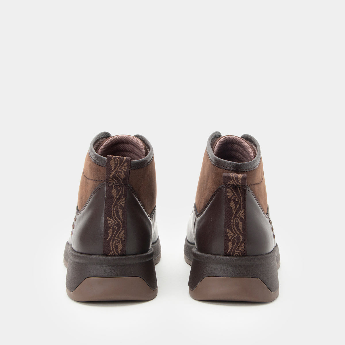 A pair of brown ankle boots shown from the back, featuring a mix of smooth and embossed leather panels with a floral pattern, set against a plain light gray background.