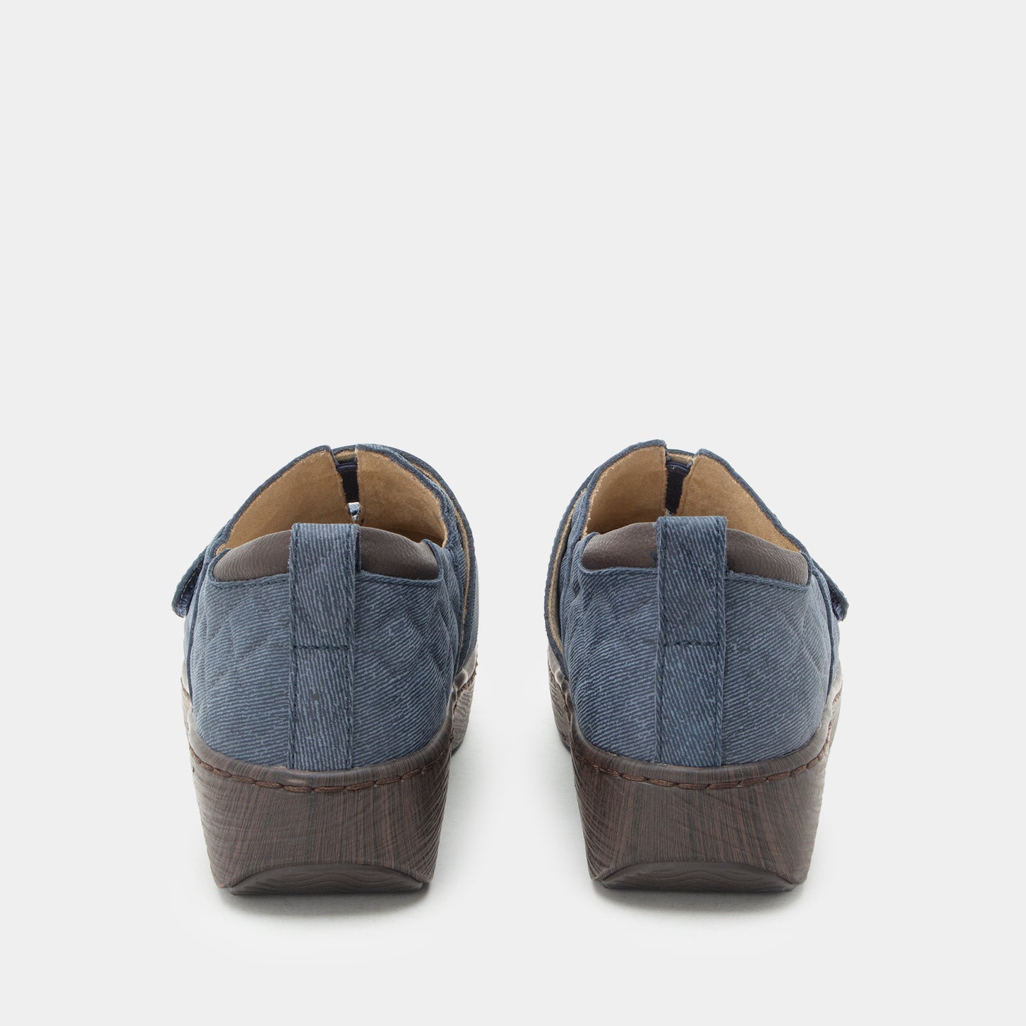A pair of women's slip-on wedge shoes shown from the back, featuring a textured blue fabric upper and a dark brown textured wedge heel, set against a plain light gray background.