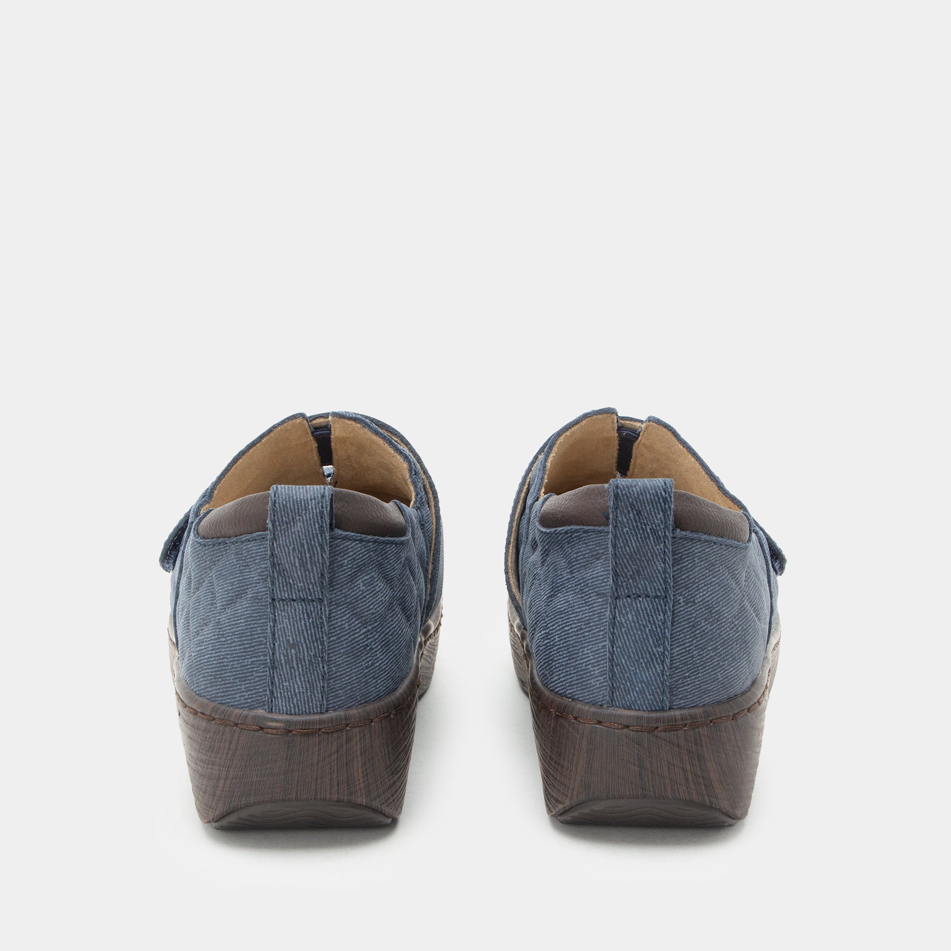A pair of women's slip-on wedge shoes shown from the back, featuring a textured blue fabric upper and a dark brown textured wedge heel, set against a plain light gray background.