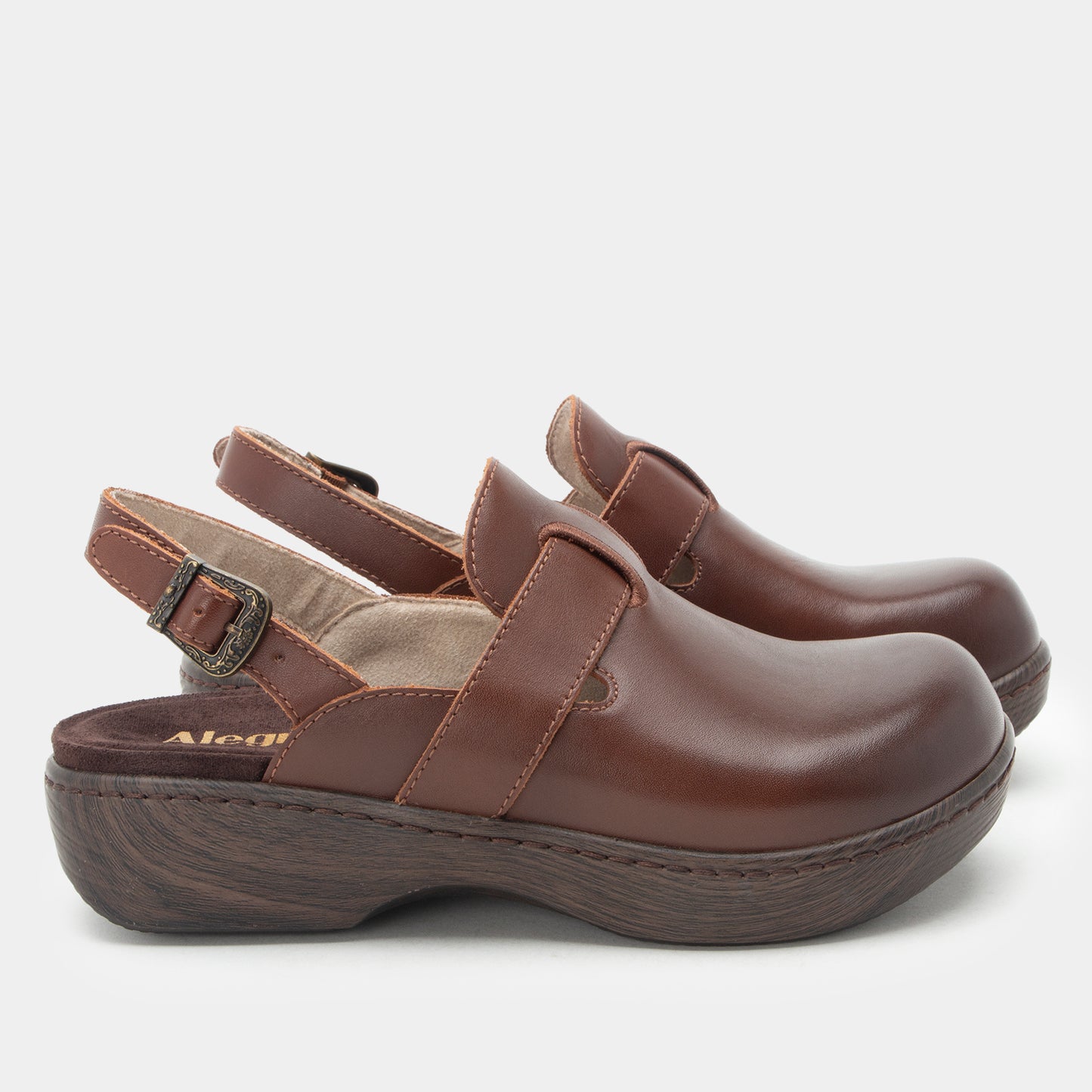 A pair of brown leather clogs with adjustable ankle straps and dark brown wedge soles, shown from a side profile on a light gray background.
