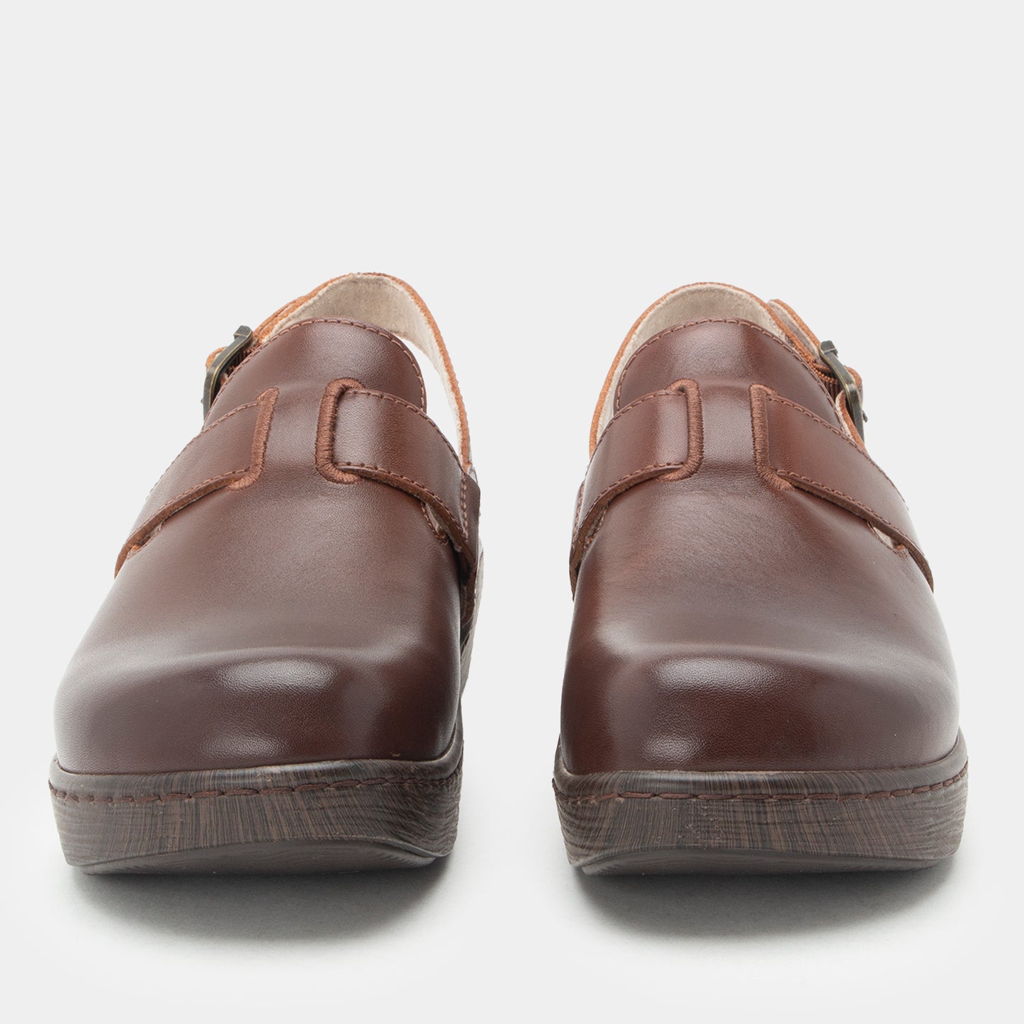 A pair of dark brown leather slip-on shoes with double straps and dark soles, photographed from the front on a light gray background.