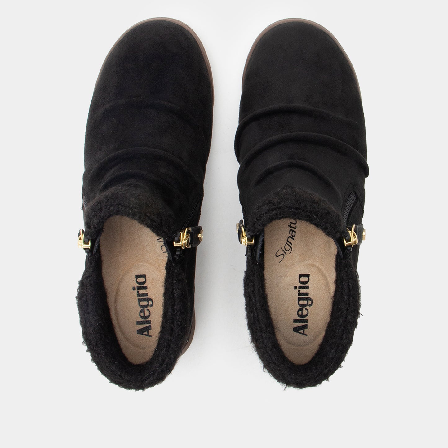 A pair of black suede ankle boots with black faux-fur lining and gold-tone hardware, shown from a top-down view on a light gray background. The insoles display the brand name 'Alegria'.
