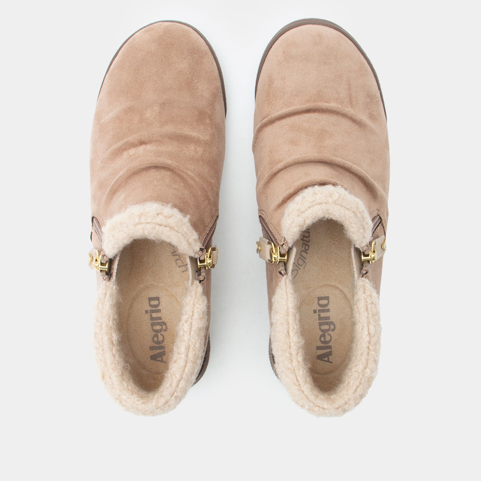 A pair of Alegría ankle boots in taupe suede with a cream sherpa lining and gold-tone buckle details, shown from a top-down view on a light gray background.