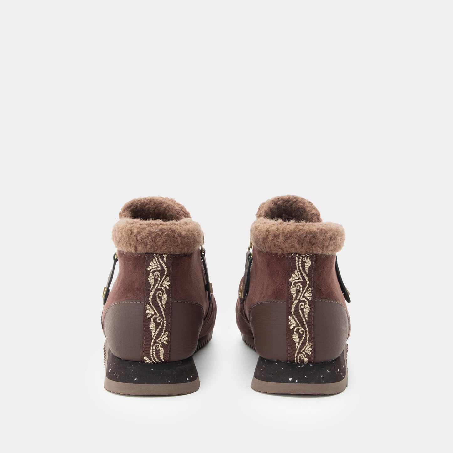 A pair of women's brown ankle boots with a plush tan shearling lining, featuring vertical cream-colored floral scroll patterns on the sides and dark brown heel panels, shown from the back against a light gray background.