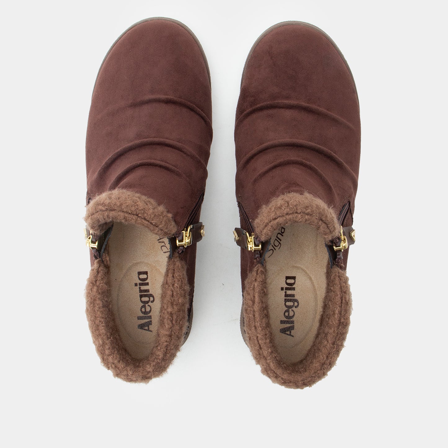 A pair of brown suede ankle boots with a plush brown shearling lining and gold-tone buckle details, shown from a top-down view on a light gray background.