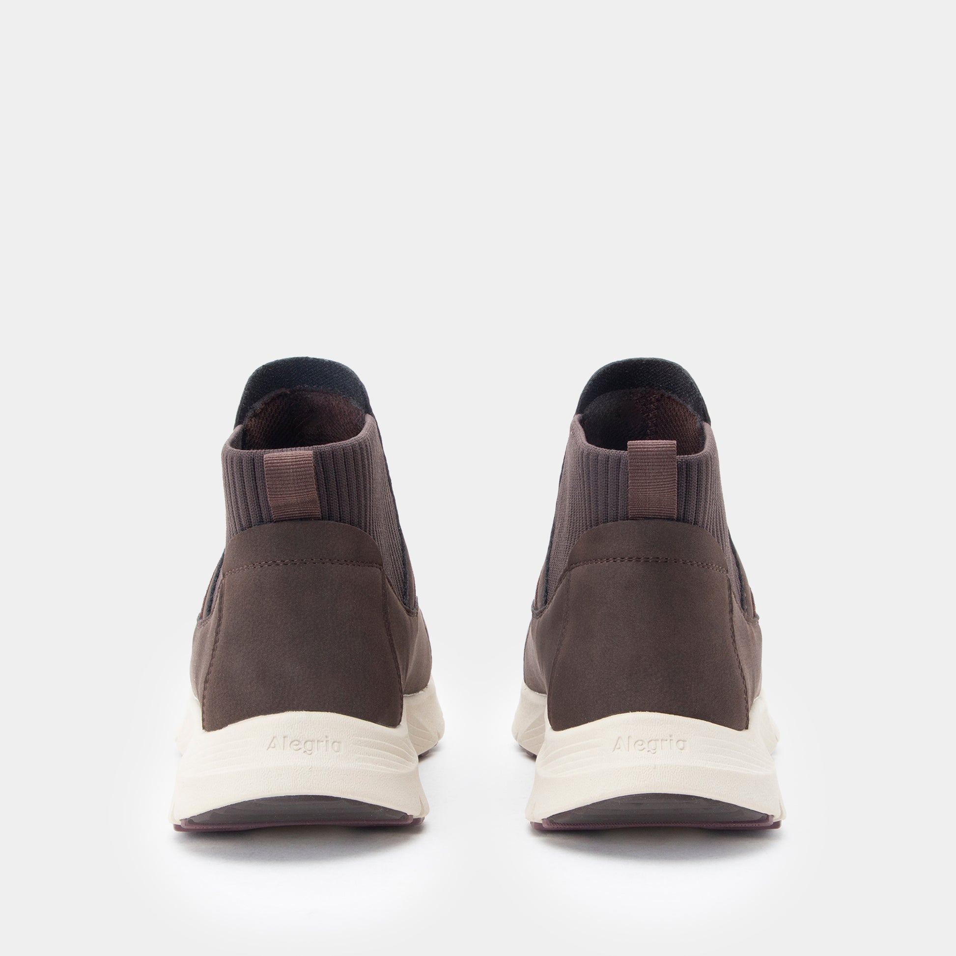 A pair of dark brown ankle-high slip-on sneakers shown from the back, featuring a textured brown upper, elastic side panels, and off-white midsoles with the brand name 'Meglis' printed on them.