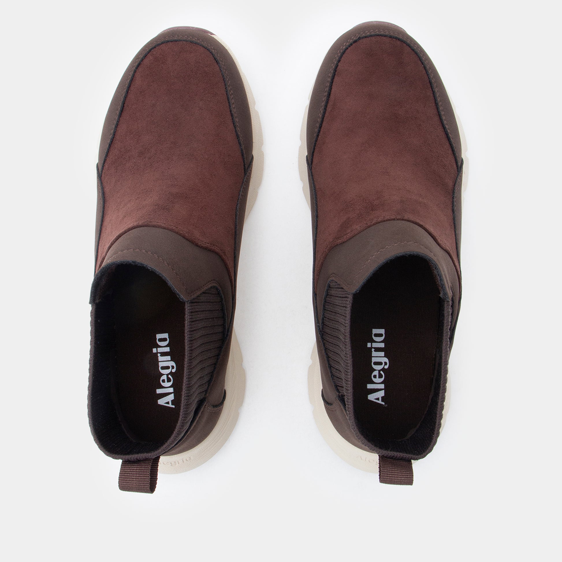 A pair of Alegria slip-on shoes in dark brown suede and dark brown elasticized trim with a white sole, shown from a top-down view on a light gray background.