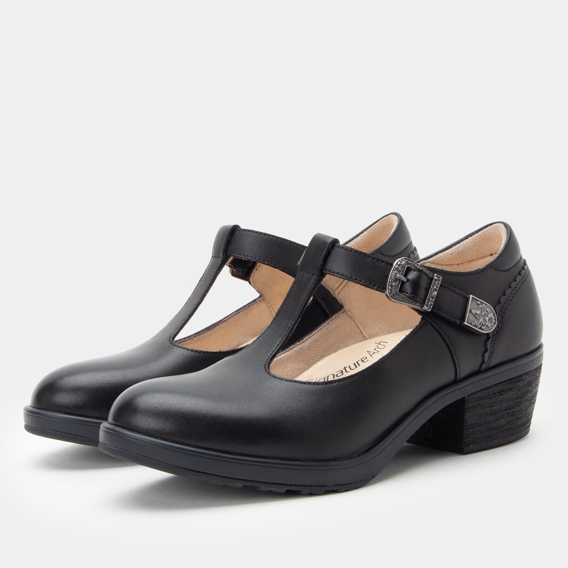 A pair of black leather Mary Jane-style shoes with a low block heel and buckle strap, shown on a light gray background.