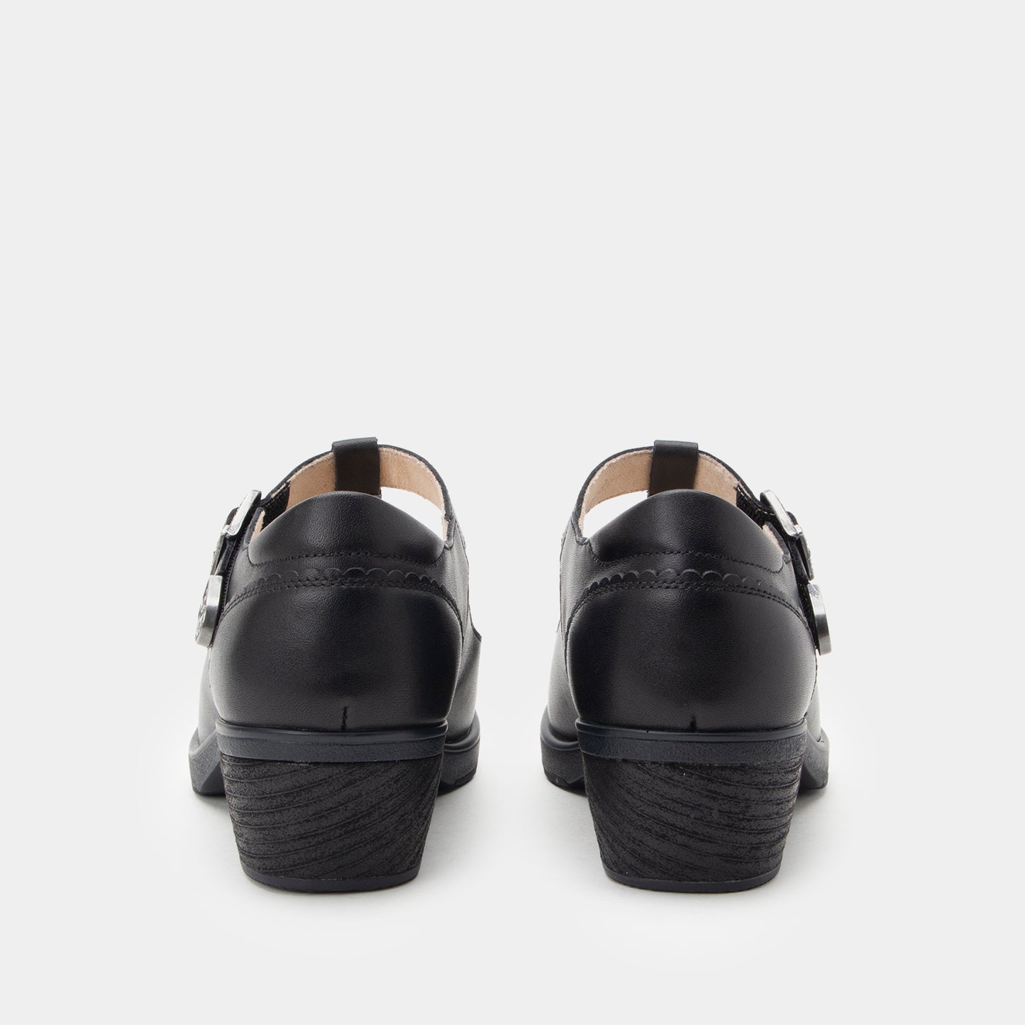 A pair of black leather Mary Jane shoes shown from the back, featuring double strap buckles and a low block heel, on a light gray background.