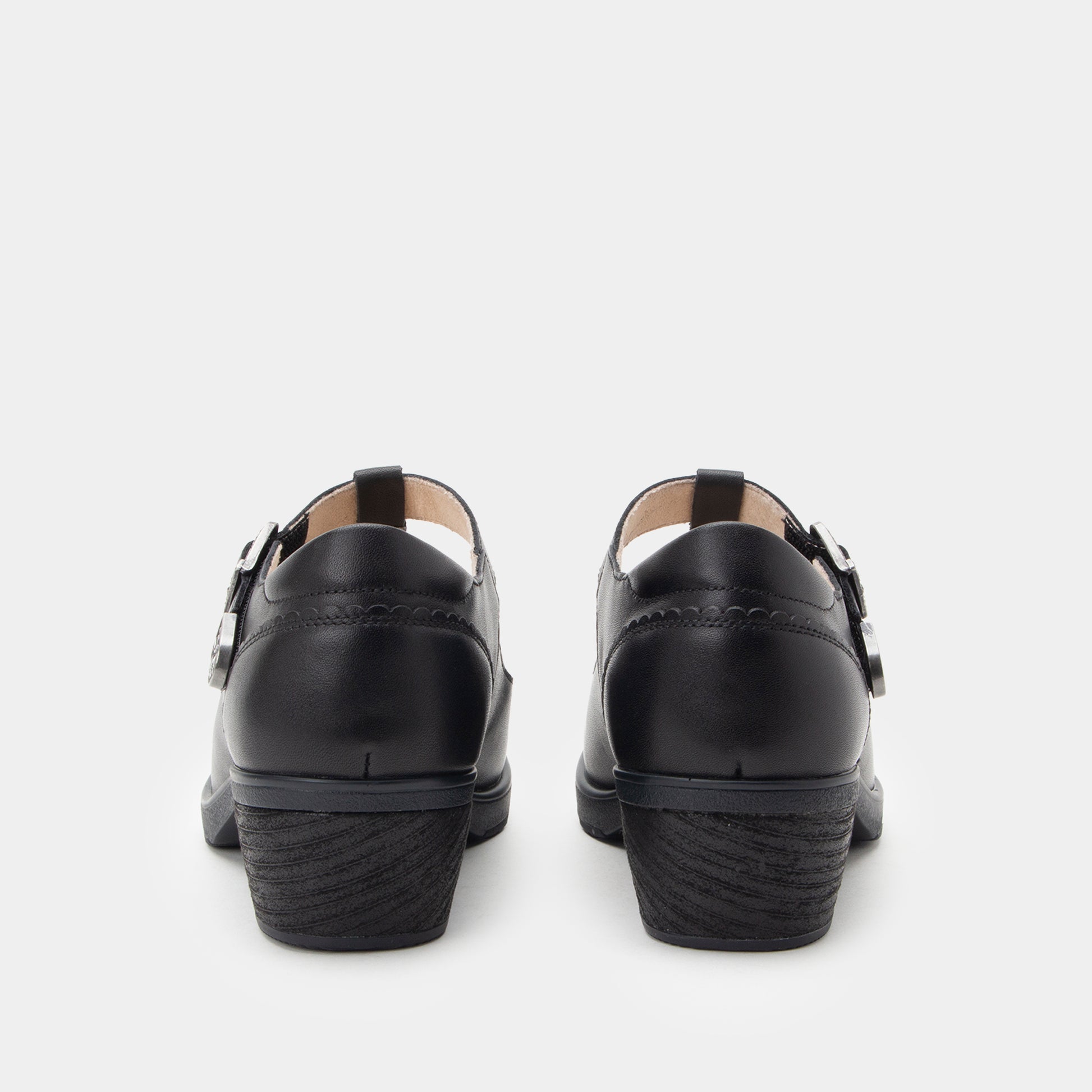 A pair of black leather Mary Jane shoes shown from the back, featuring double strap buckles and a low block heel, on a light gray background.