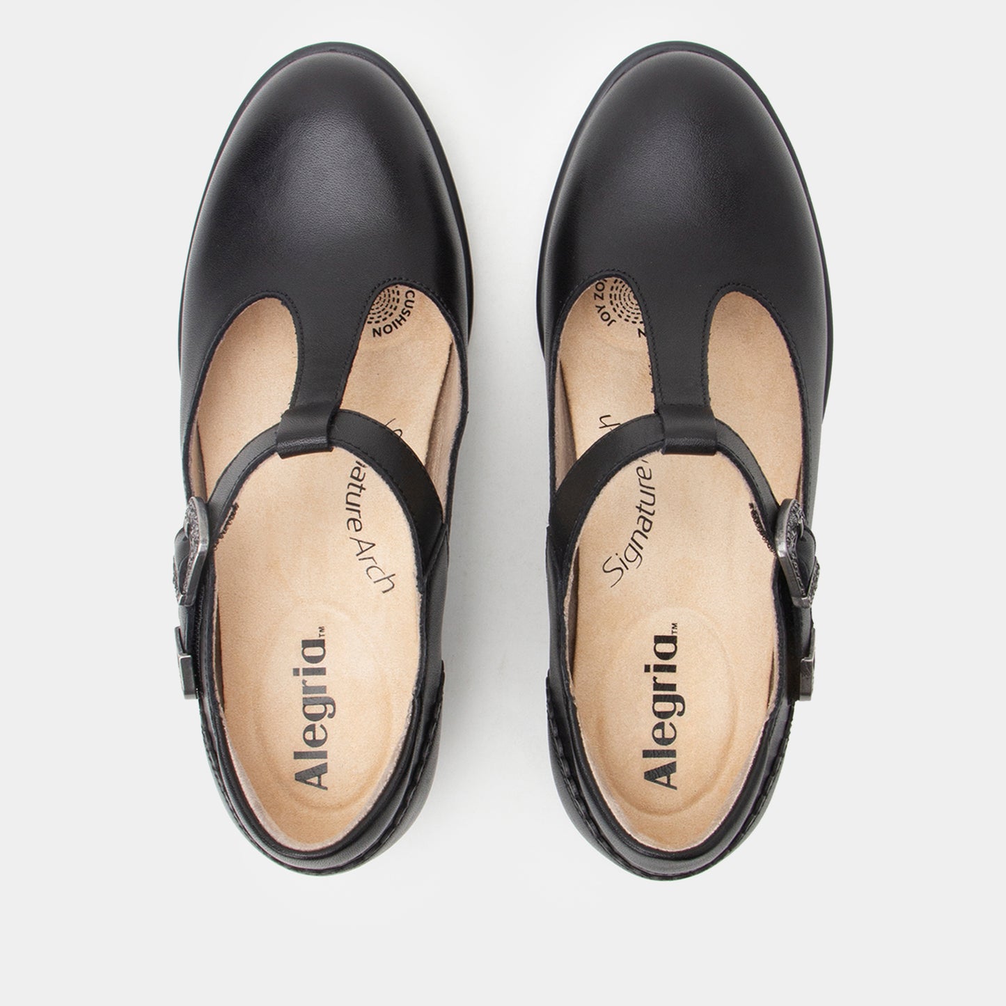 A pair of black leather T-strap Mary Jane shoes shown from a top-down view on a light gray background. The insoles are beige with the brand name 'Alegria' and 'Signature' printed on them.