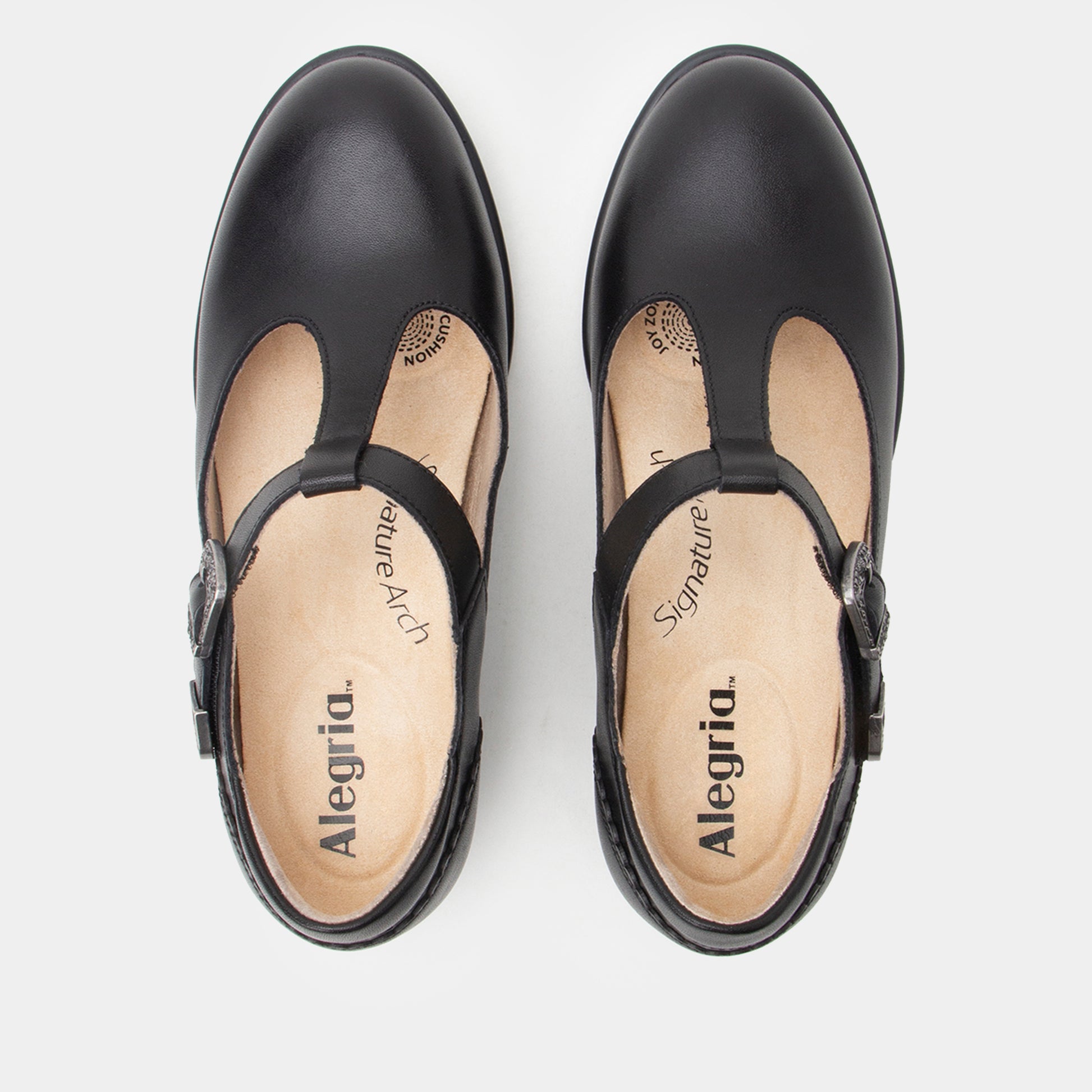 A pair of black leather T-strap Mary Jane shoes shown from a top-down view on a light gray background. The insoles are beige with the brand name 'Alegria' and 'Signature' printed on them.