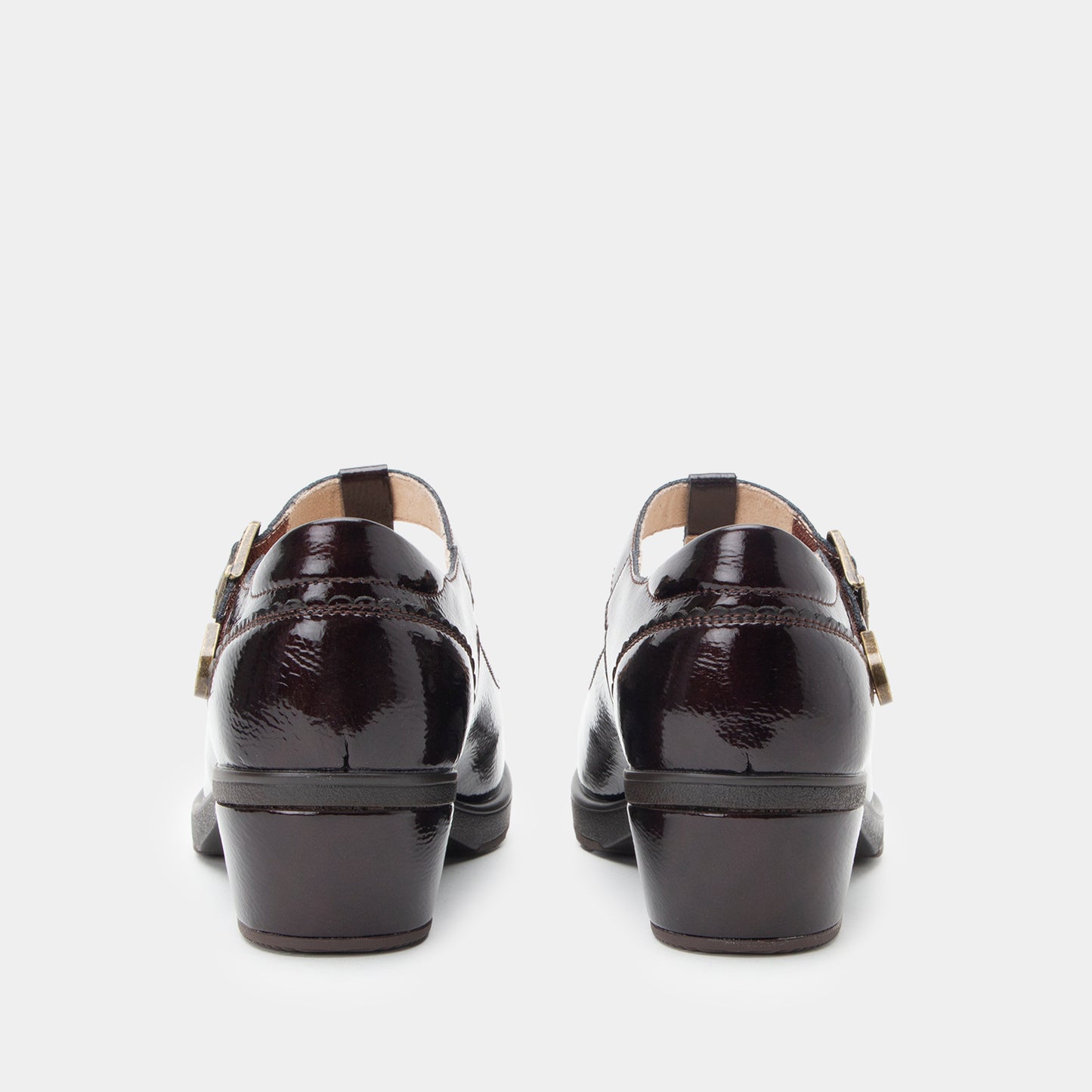 A pair of black patent leather Mary Jane shoes shown from the back, featuring low block heels and decorative gold-tone buckle straps, set against a plain light gray background.