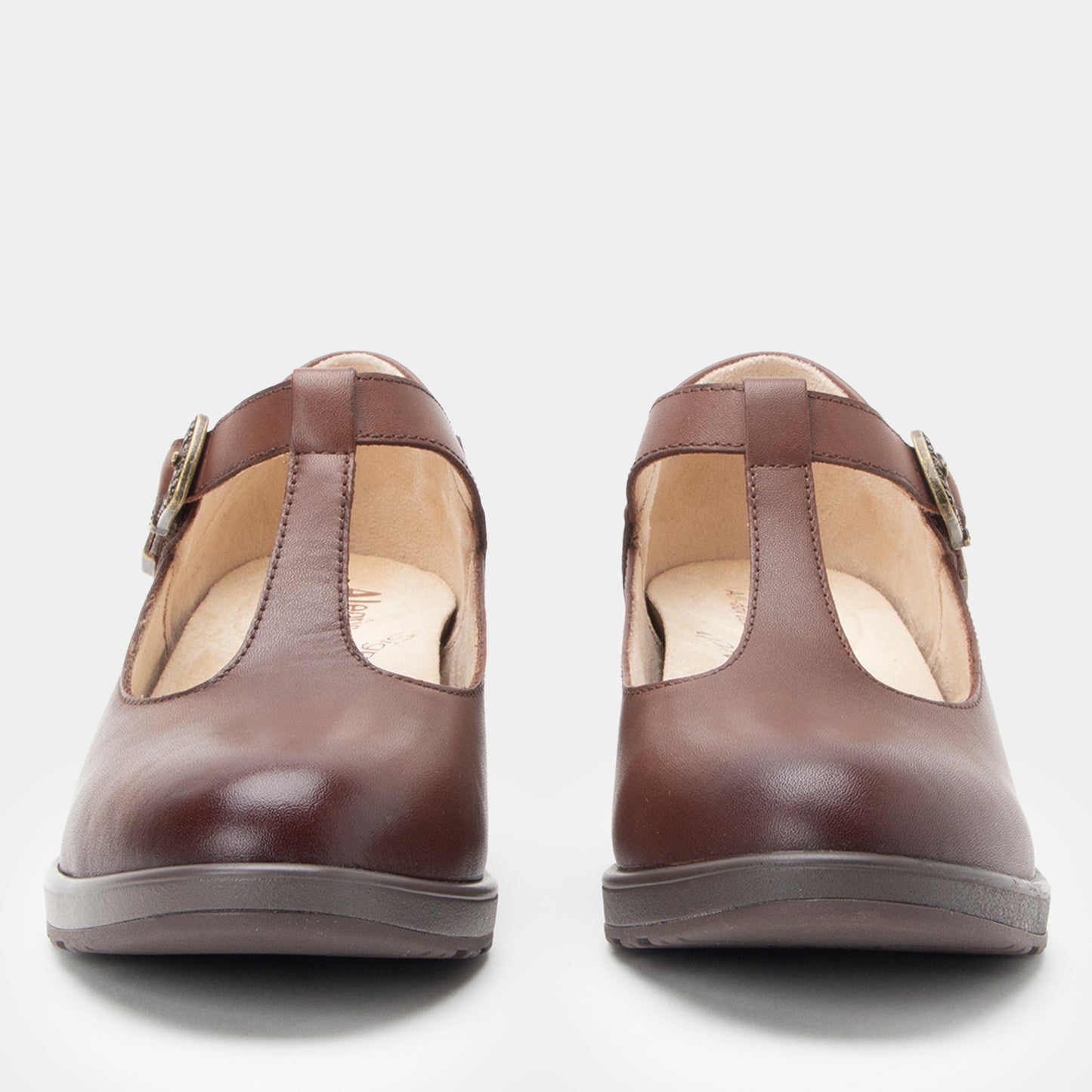 A pair of dark brown leather Mary Jane shoes with buckle straps, shown from the front against a light gray background.